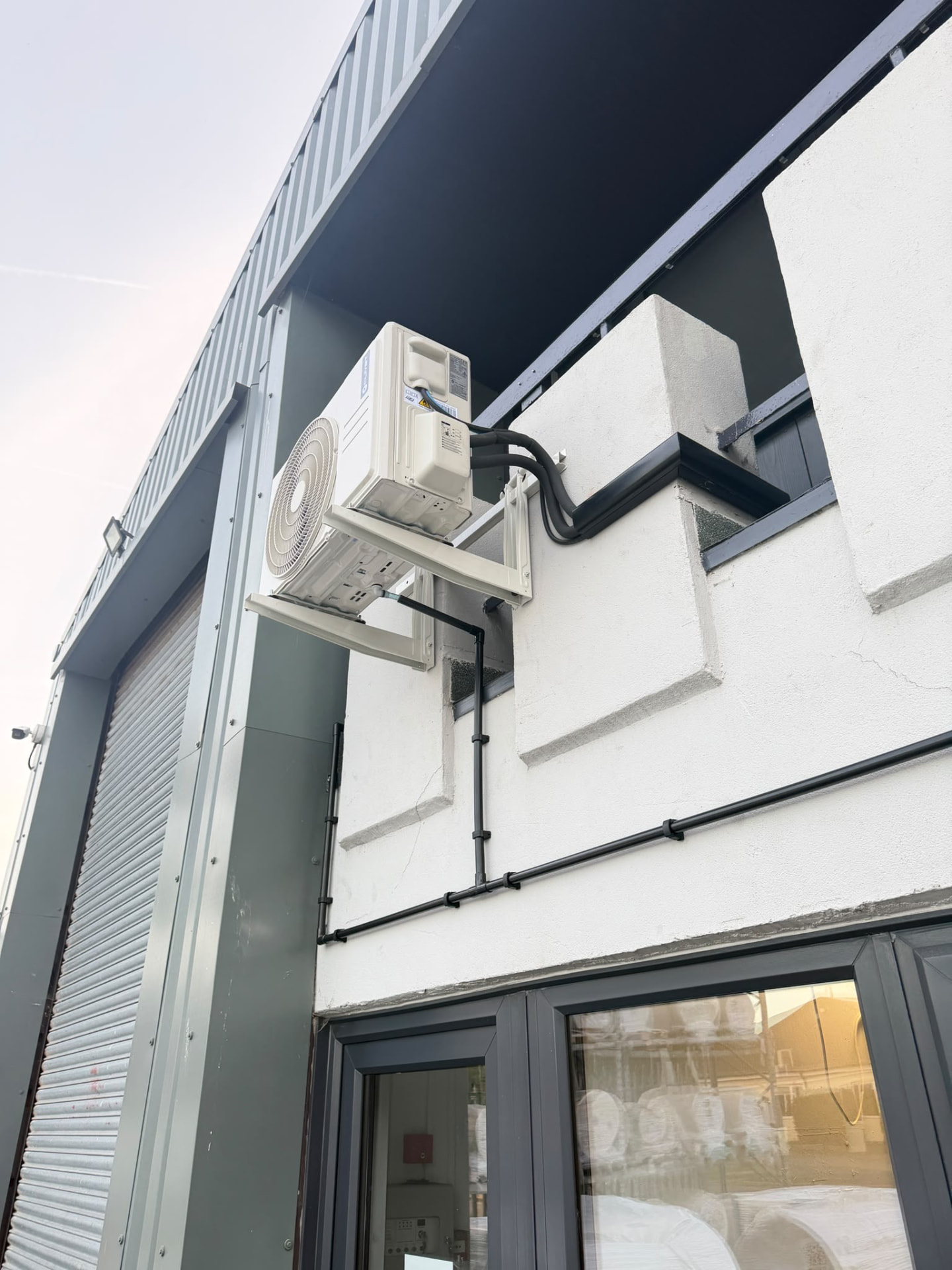 Outdoor unit on a wall bracket above the balcony with black trunking running along the building