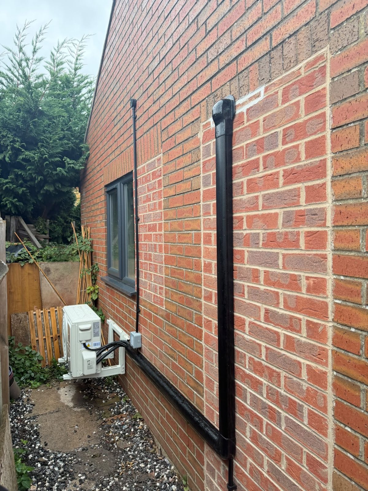 Side view of the brick garden room showing the outdoor unit on its wall bracket and the black trunking route