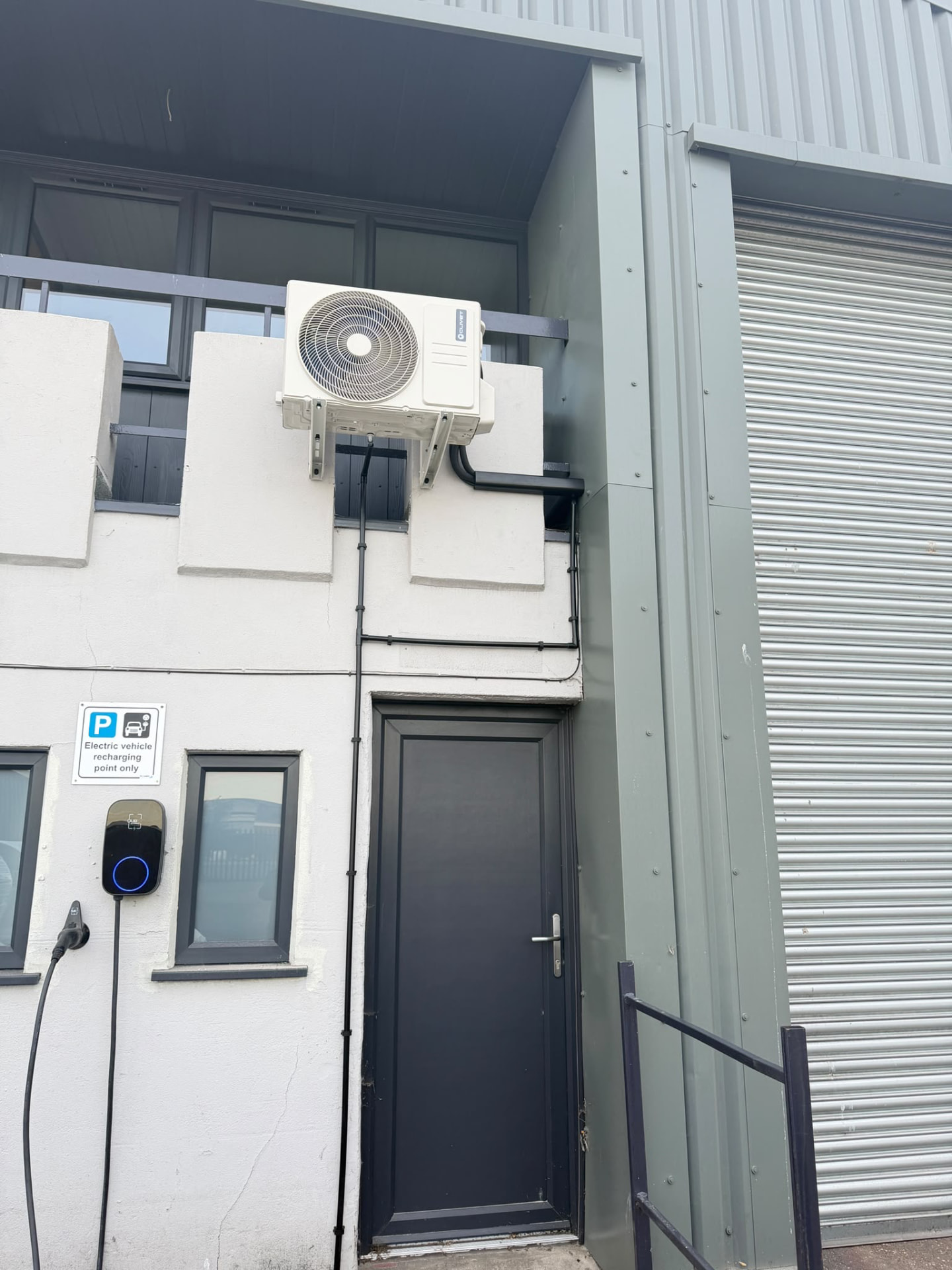 Second Clivet outdoor unit on a wall bracket above a door, with black trunking beside an electric vehicle charging point